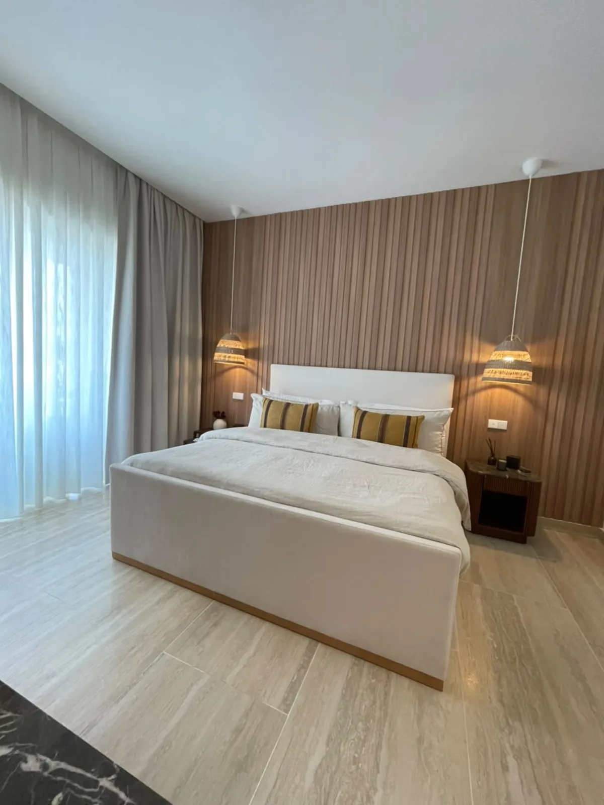 Photographie de la chambre principale de la résidence témoin : lit tapissé contre une boiserie cannelée, une suspension de chaque côté.