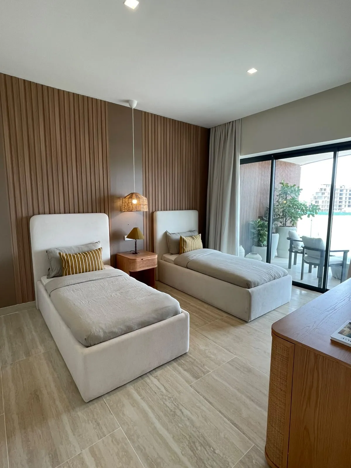Photographie de la deuxième chambre de la résidence témoin : deux lits simples, boiserie cannelée, portes ouvrant sur la terrasse.
